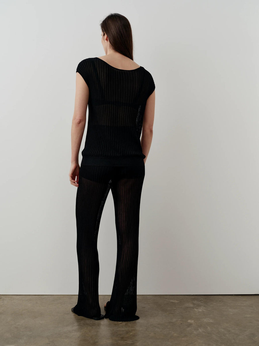 Woman wearing Emello Plissé Boat Neck Top, semi-sheer black knit with a fluid drape, viewed from behind.