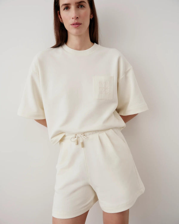 Cream embroidered pocket shorts with relaxed fit, worn by woman standing against a white background.