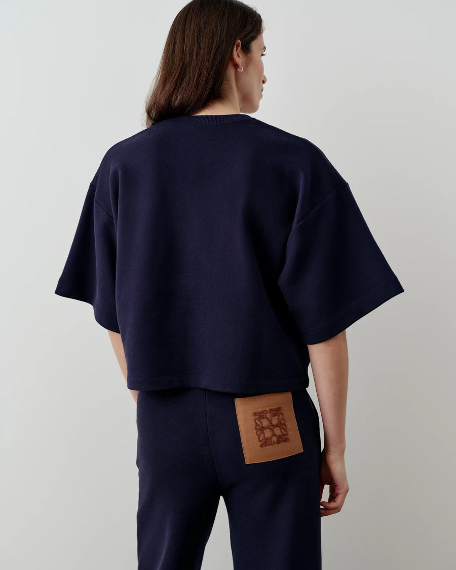 Model wearing Emello's short sleeve navy sweatshirt with a relaxed, boxy shape, showcasing the back with tonal stitching and dropped shoulders.