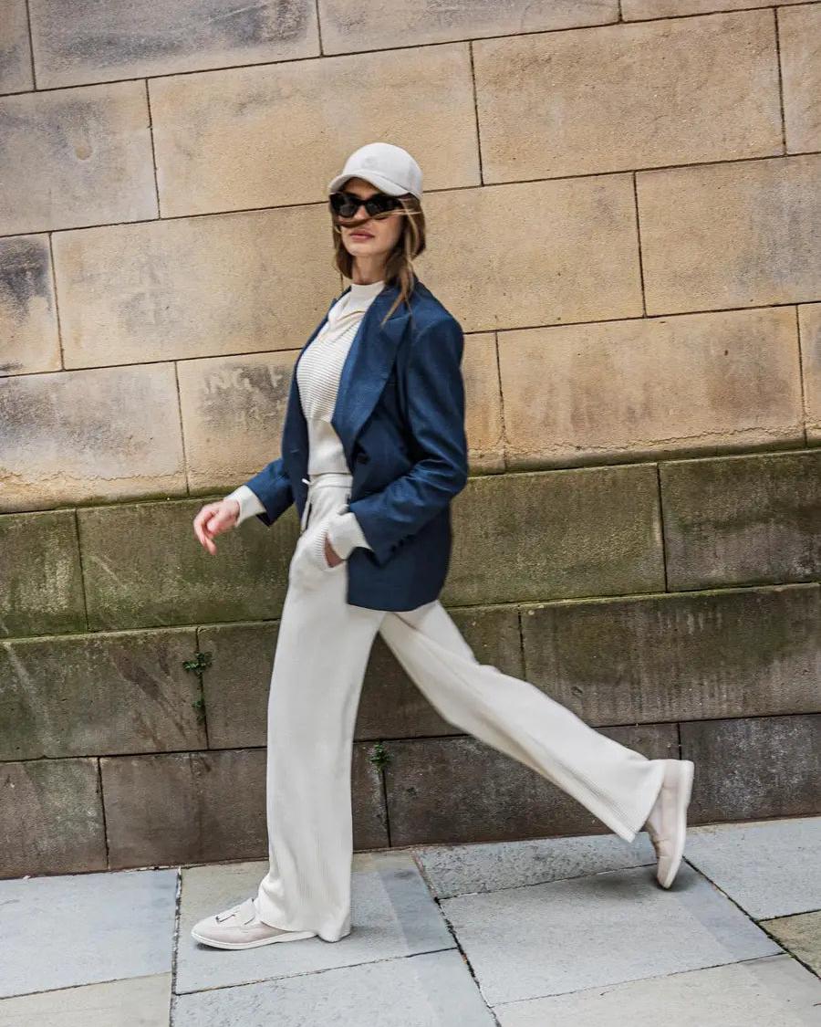 Woman in cream knit pants, ribbed top, and navy blazer walking confidently in an urban setting