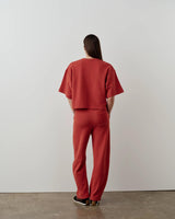 Rear view of a model wearing Emello Relaxed Straight Leg Trousers in muted rust-red.