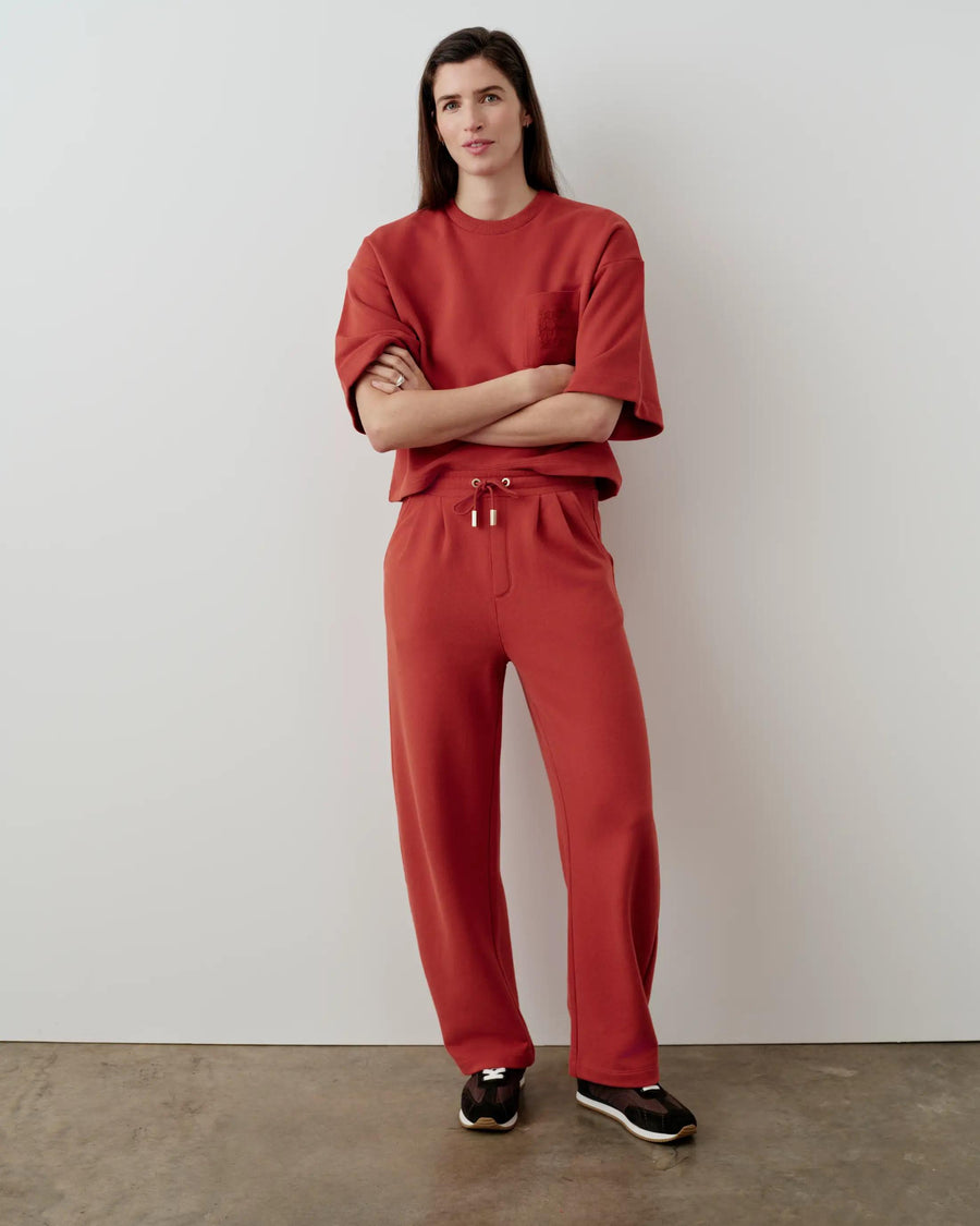 Model wearing relaxed straight leg trousers in muted rust-red with a matching top.