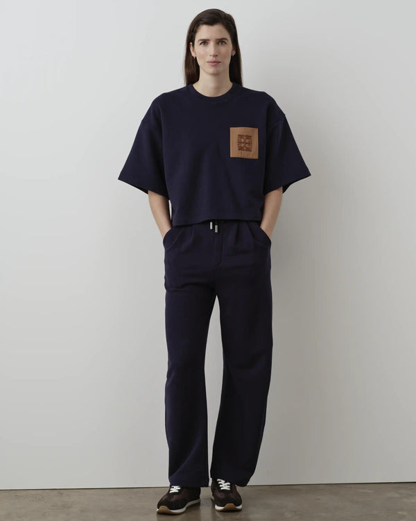 Model wearing Emello's navy short sleeve pocket sweatshirt with relaxed and boxy silhouette, featuring a twill chest pocket and chain-stitch embroidery.