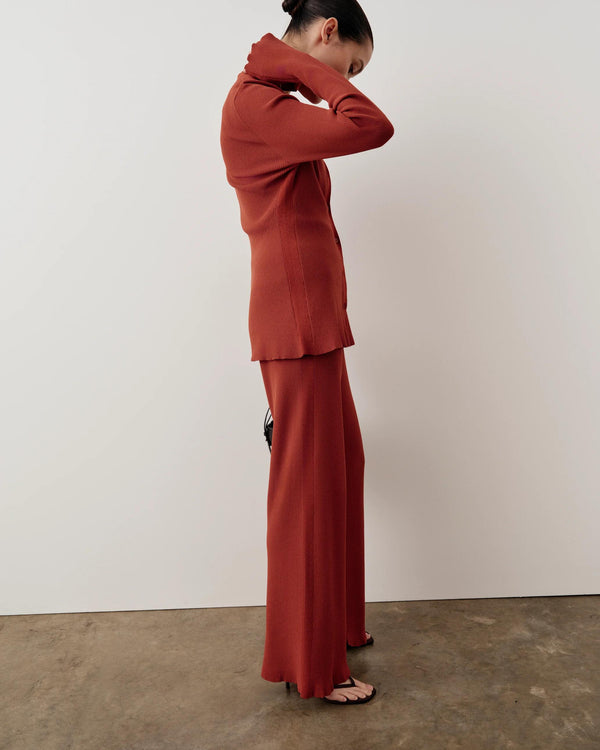 Side profile of a woman wearing a rust red tonal ribbed cardigan with elongated sleeves and button closure.
