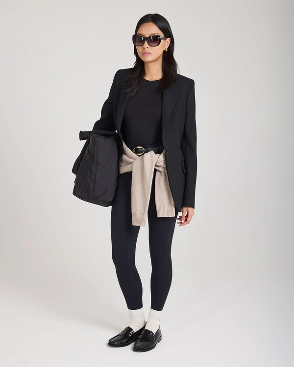 Elegant woman wearing cream ribbed cotton half-crew socks with embroidery, black blazer, black leggings, and loafers.