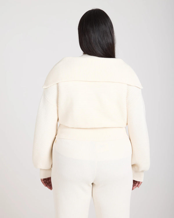 Back view of a cream-colored ribbed half zip jumper worn by a model, showcasing a relaxed fit and tactile elegance.