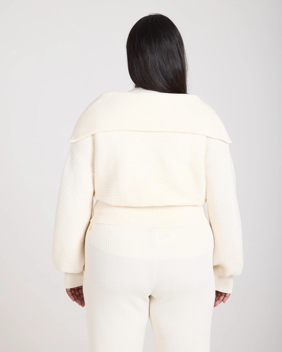Back view of a cream-colored ribbed half zip jumper worn by a model, showcasing a relaxed fit and tactile elegance.