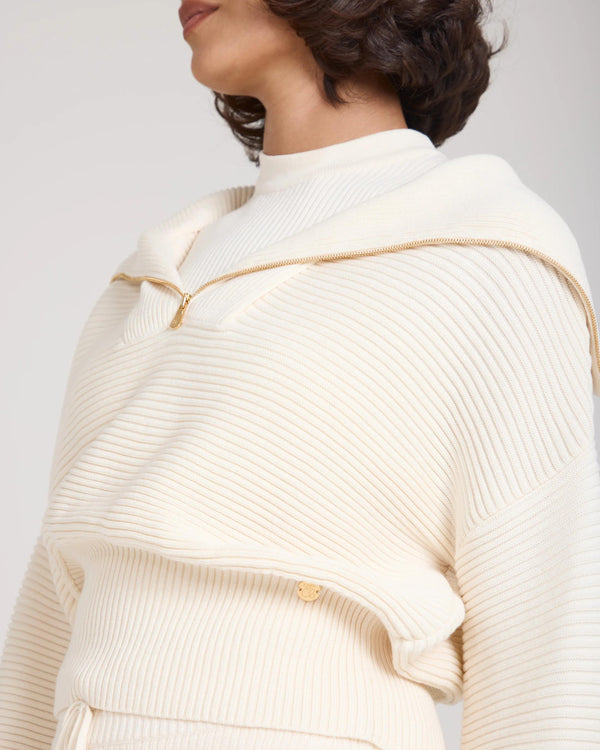Close-up of a cream ribbed half zip jumper with gold accents, elegant and refined.