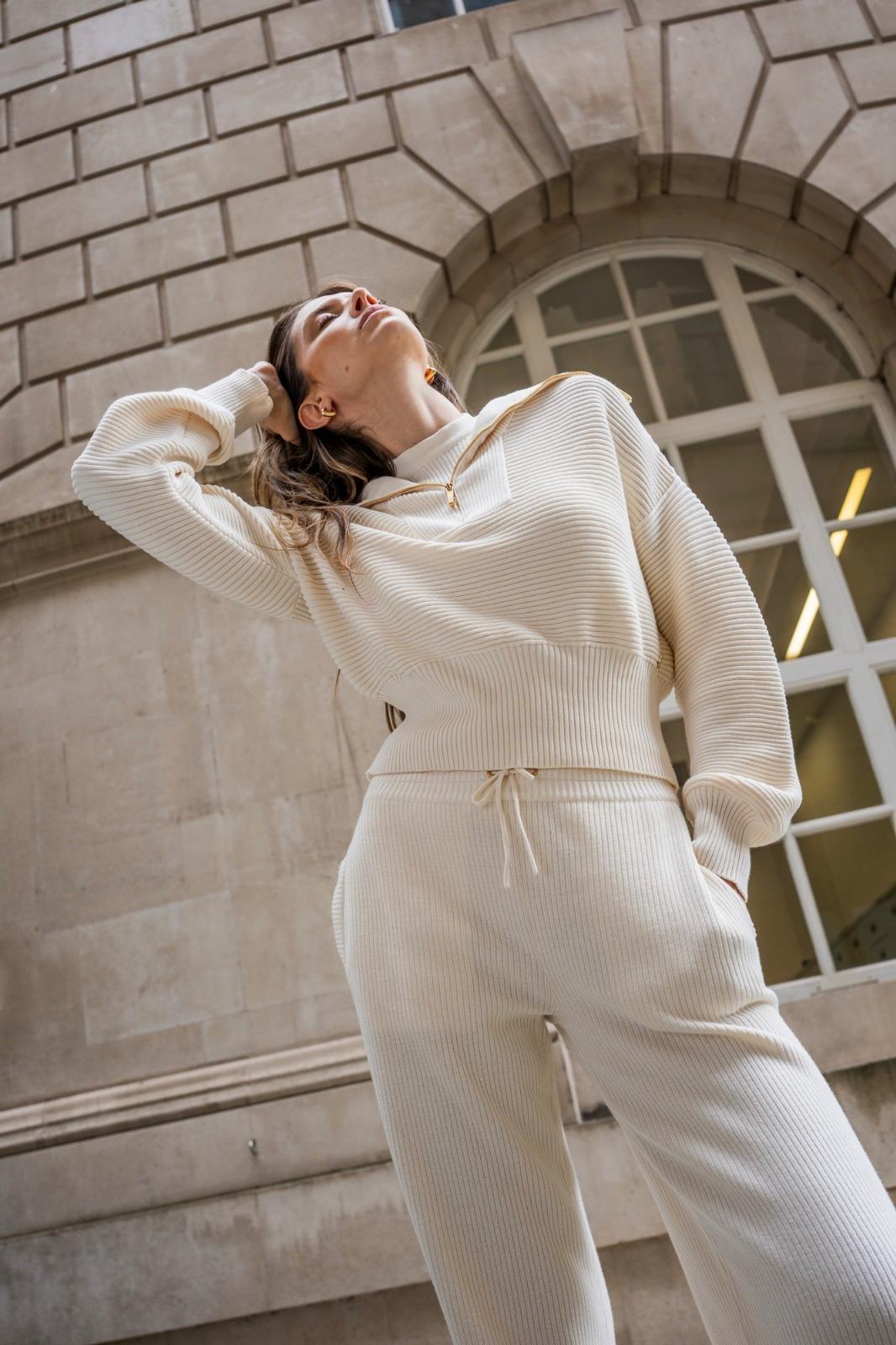 Woman in cream ribbed knit lounge set, gazing upward against a stone building backdrop