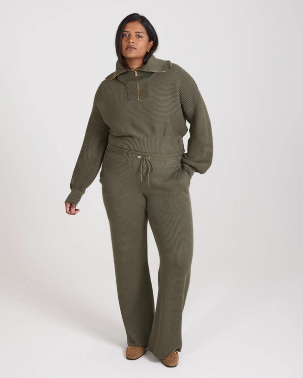 Model wearing Emello Sorella Ribbed Knit Wide Leg Trousers in Olive, showcasing relaxed fit and gold-finish details.