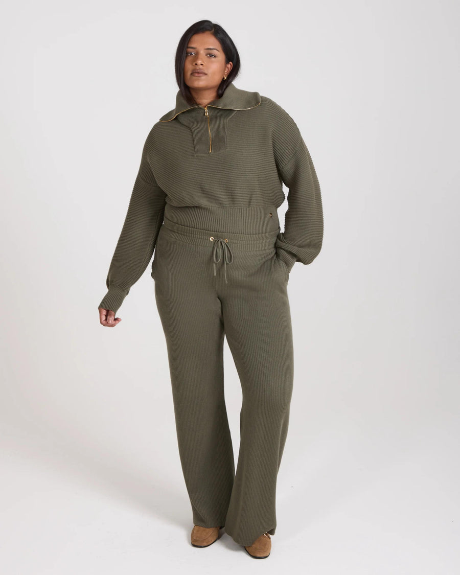 Model wearing Emello Sorella Ribbed Knit Wide Leg Trousers in Olive, showcasing relaxed fit and gold-finish details.