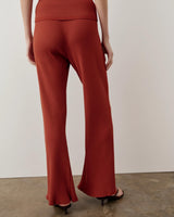 Back view of Emello's tonal ribbed knit trousers in warm rust red, showcasing a fluid, wide-leg silhouette.