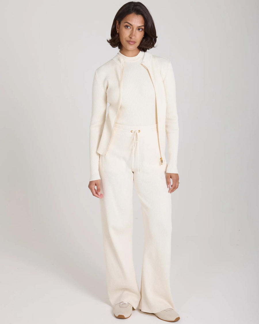 Model wearing cream ribbed knit wide leg trousers and matching top in a relaxed and elegant style.