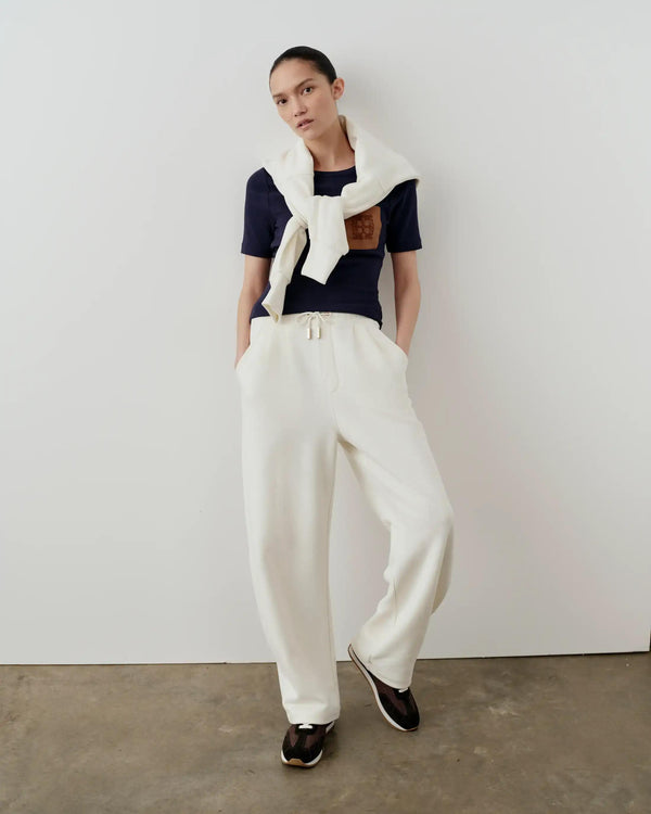 Model wearing Emello navy ribbed pocket tee with elegant drape, paired with white pants against a minimalist backdrop.