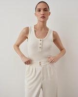Model wearing Emello cream ribbed popper tank top with pleated trousers.