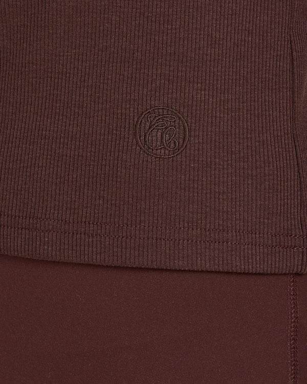 Close-up of Emello's chocolate brown ribbed turtleneck showing the fine texture and subtle emblem embroidery.