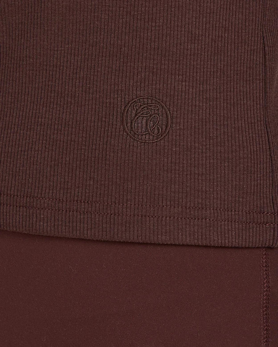 Close-up of Emello's chocolate brown ribbed turtleneck showing the fine texture and subtle emblem embroidery.