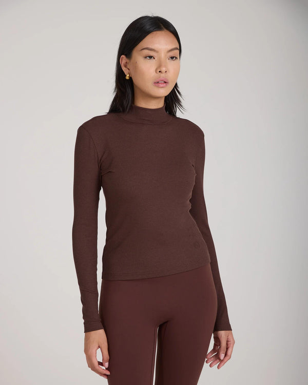 Emello Forma Ribbed Lyocell-Cotton Blend Turtleneck Top in Chocolate, worn by a model gracefully standing with neutral expression in soft studio light.