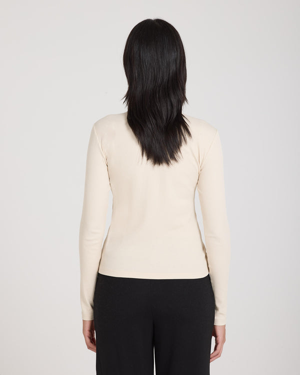 Back view of a women's beige ribbed turtleneck top, long-sleeved, worn with black trousers.