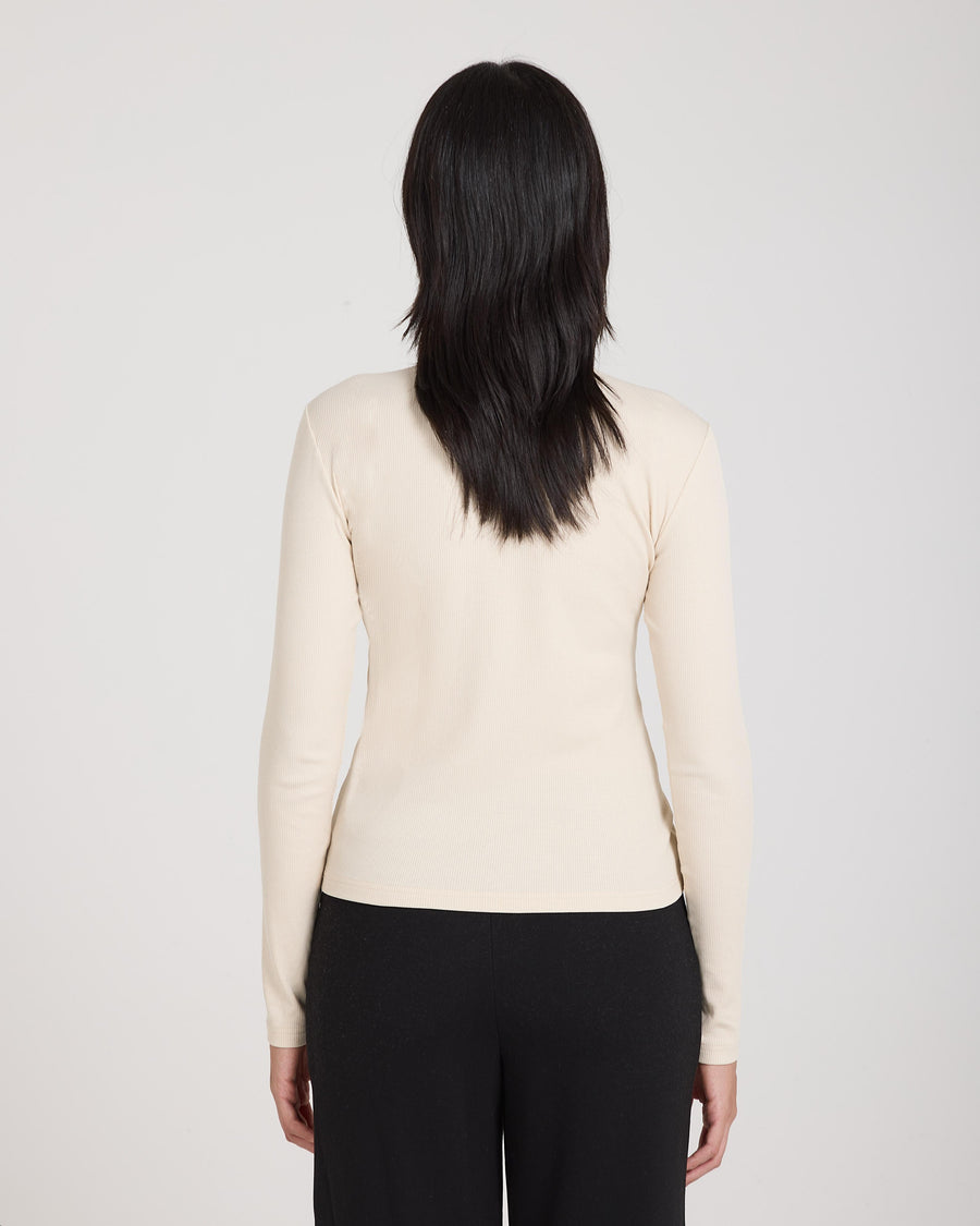 Back view of a women's beige ribbed turtleneck top, long-sleeved, worn with black trousers.
