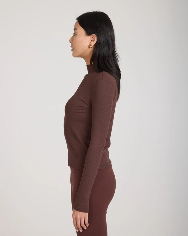 Side view of a woman wearing a chocolate brown ribbed turtleneck top by Emello, highlighting its slim fit and high collar.
