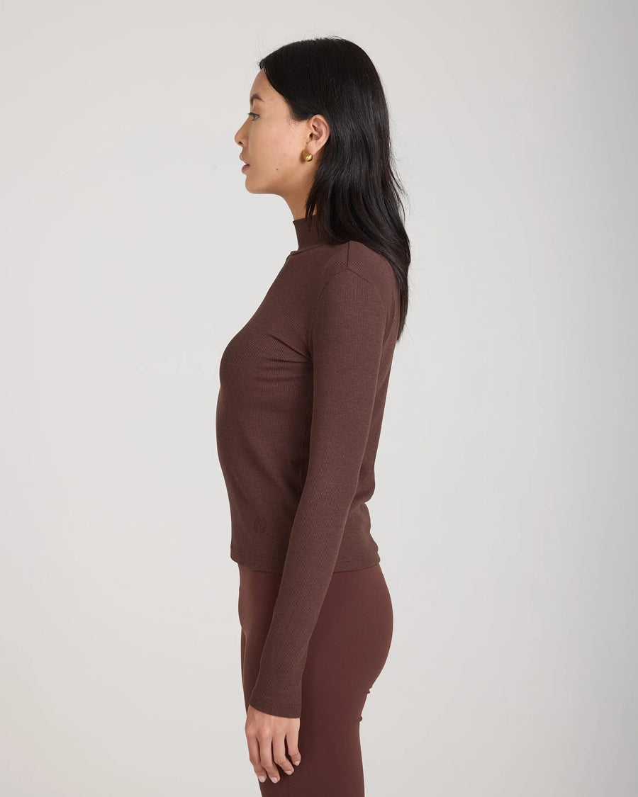 Side view of a woman wearing a chocolate brown ribbed turtleneck top by Emello, highlighting its slim fit and high collar.