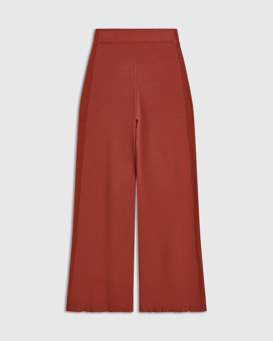 Tonal Ribbed Knit Trousers in warm rust red, showcasing elongated silhouette and sculpted line.