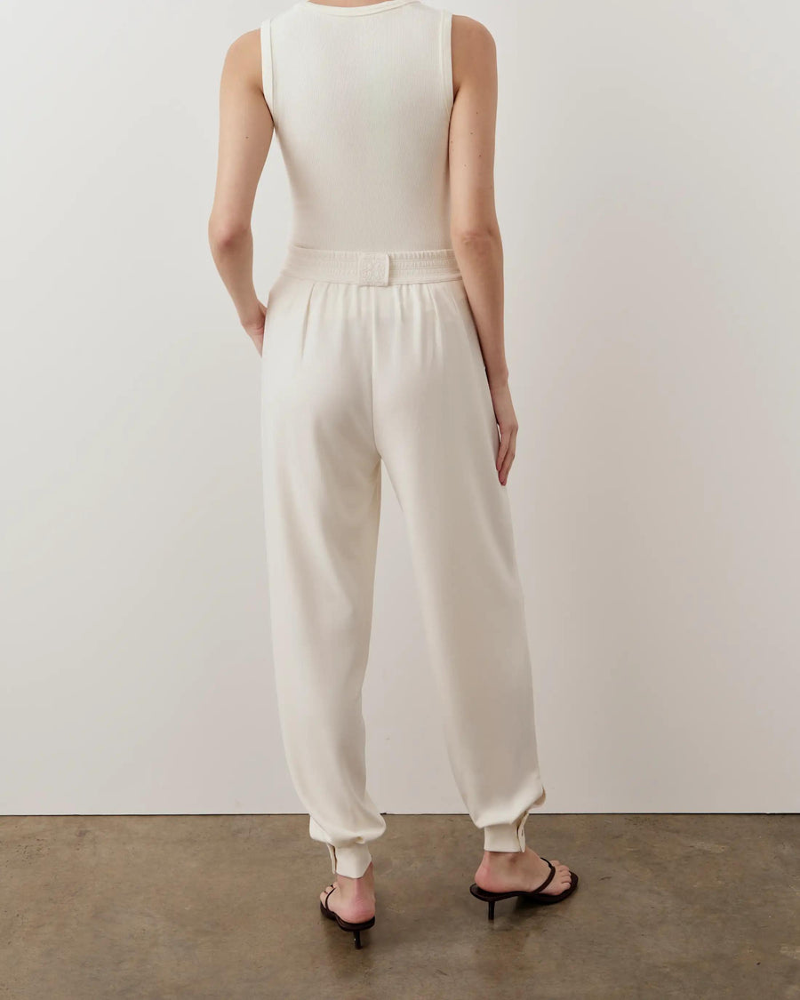 Back view of a woman wearing a cream ribbed popper tank top, showcasing its elegant, body-skimming fit.