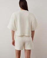 Back view of a cream short-sleeve pocket sweatshirt, showcasing the relaxed, boxy fit and elegant simplicity.
