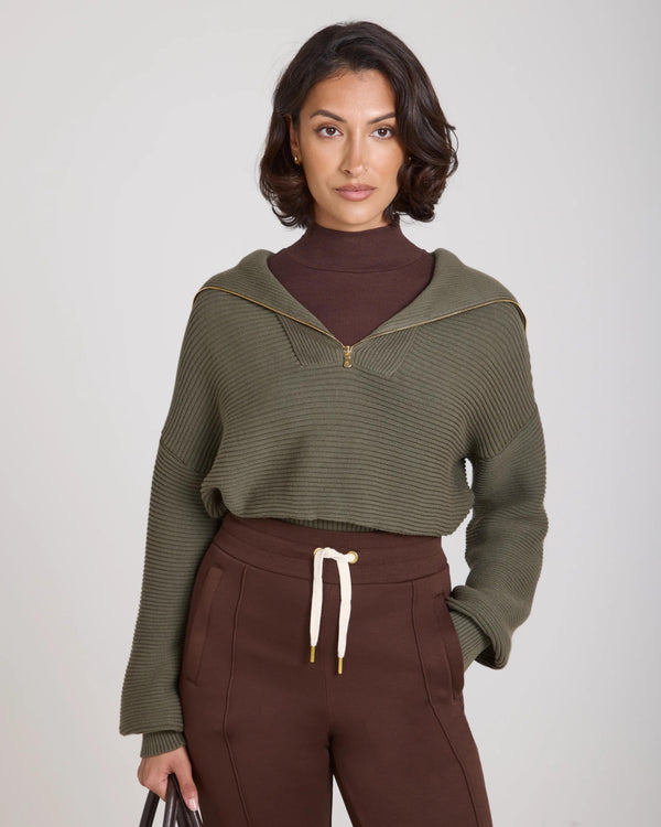 Model wearing Emello Sorella Ribbed Half Zip Jumper in Olive, showcasing its sculptural silhouette and gold accents.