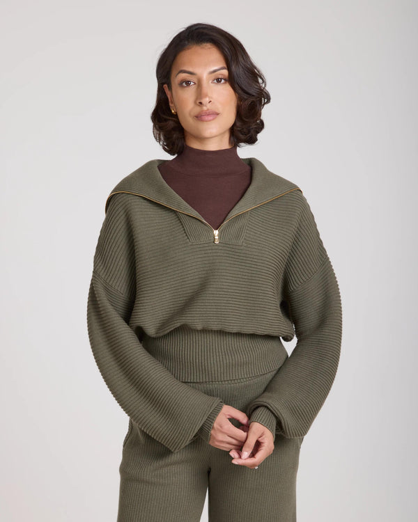 Model wearing the Sorella Ribbed Half Zip Jumper in Olive, showcasing its relaxed silhouette and gold zip detailing.