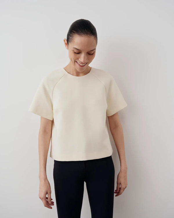 Model wearing a cream structured short sleeve top with a sculptural silhouette by Emello.