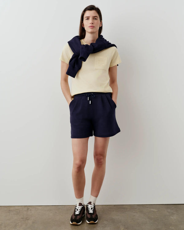 Model wearing Emello Supima Cotton Pocket Tee in butter yellow, paired with navy shorts, conveying a sense of elevated casual elegance.