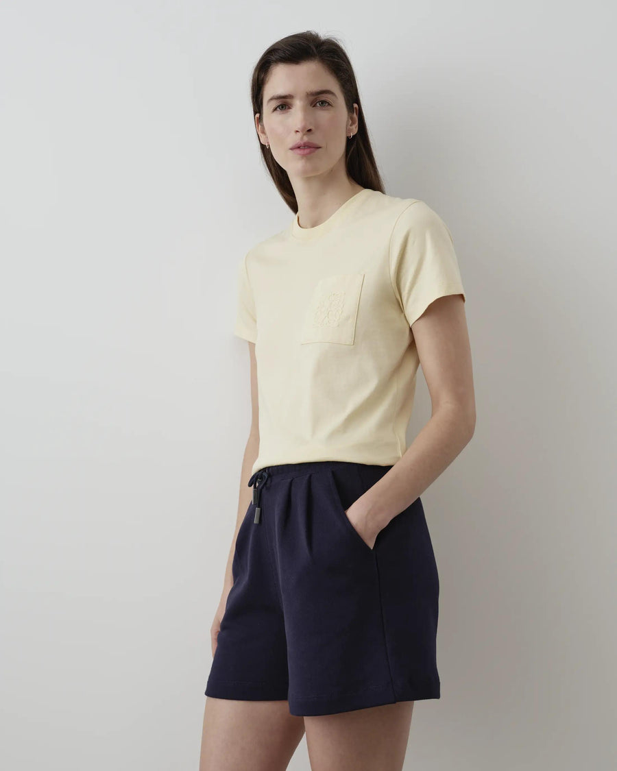 Model wearing Emello Supima Cotton Pocket Tee in butter yellow, styled with navy shorts.