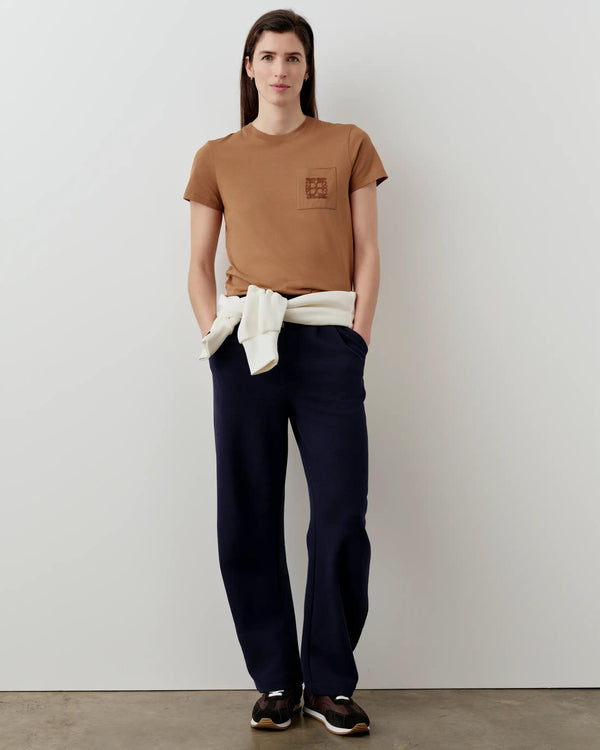 Supima Cotton Pocket Tee in camel brown with Emello's signature mirror chain-stitch embroidery, worn by a model with navy pants and sneakers.