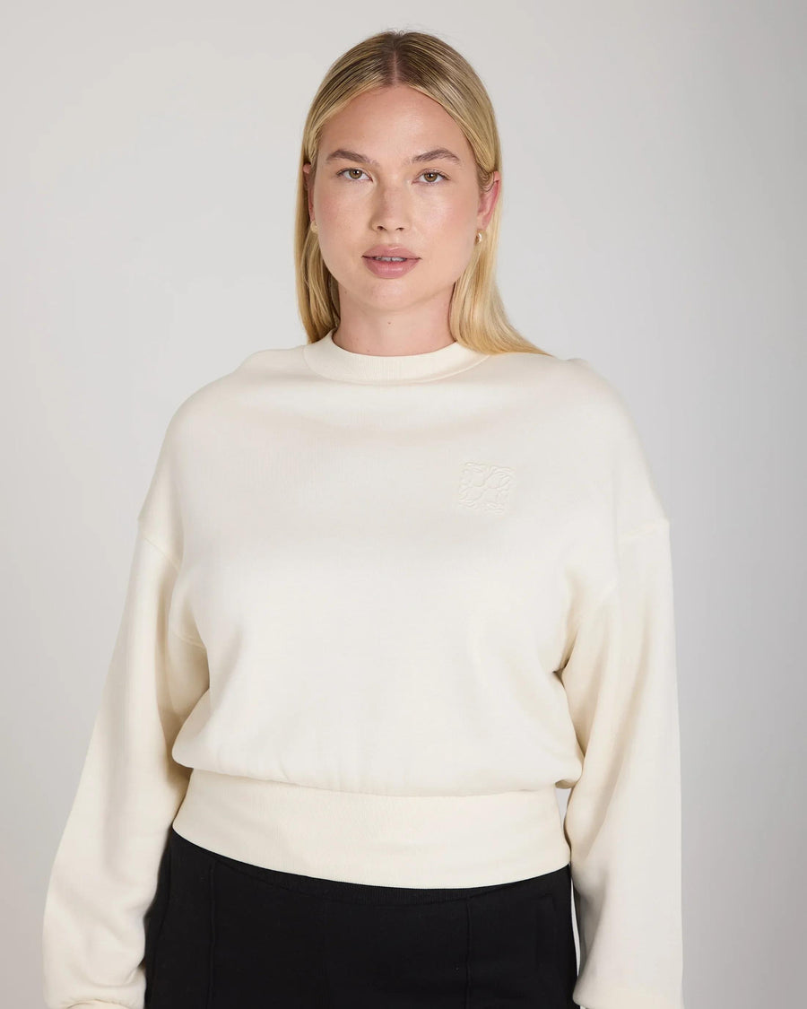 Cream sweatshirt with debossed logo in super-soft lyocell fleece, worn by a model with relaxed confidence.