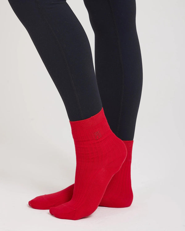 Red ribbed cotton half-crew socks with a subtle embroidered emblem and reinforced heel and toe, worn by a model.