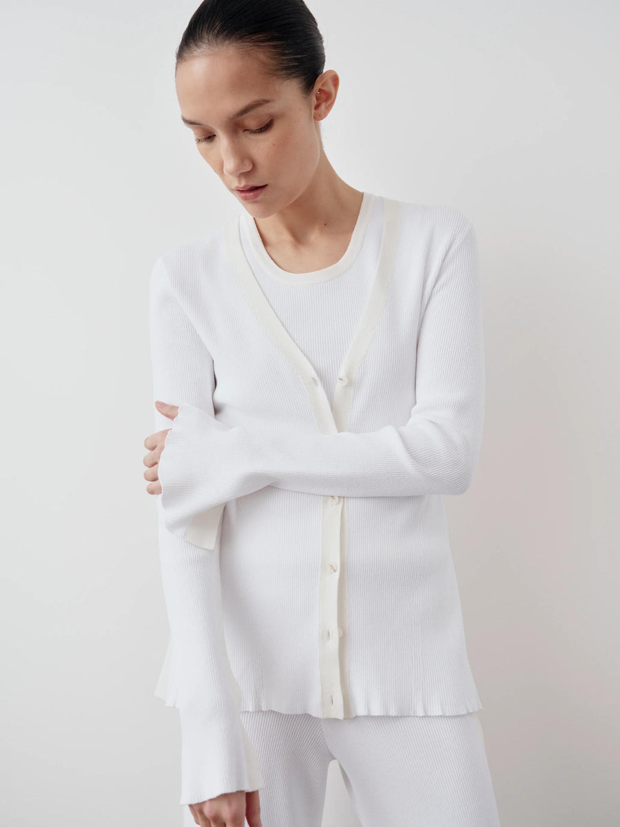 Emello Tonal Ribbed Cardigan with a clean V neckline, worn by a model, showcasing its elegant fluted cuffs and waved edges in soft white.