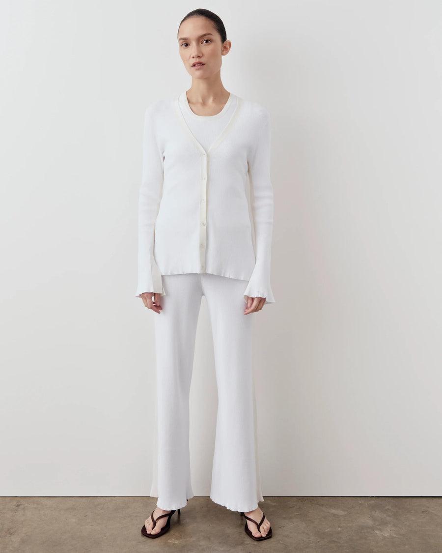 White tonal ribbed cardigan with fluted cuffs and V-neckline, worn by a model standing against a white background.