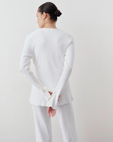 Back view of a model wearing Emello's white tonal ribbed cardigan, showcasing its sculpted fit and elegant fluted cuffs.