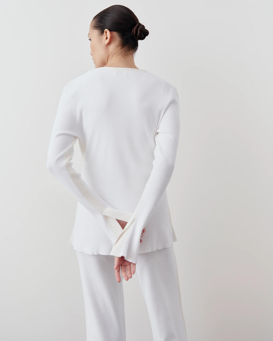 Back view of a model wearing Emello's white tonal ribbed cardigan, showcasing its sculpted fit and elegant fluted cuffs.