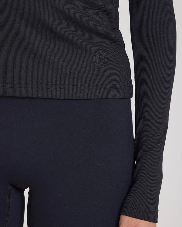 Close-up of Emello's black Forma ribbed turtleneck top highlighting the intricate textured fabric and slim fit.