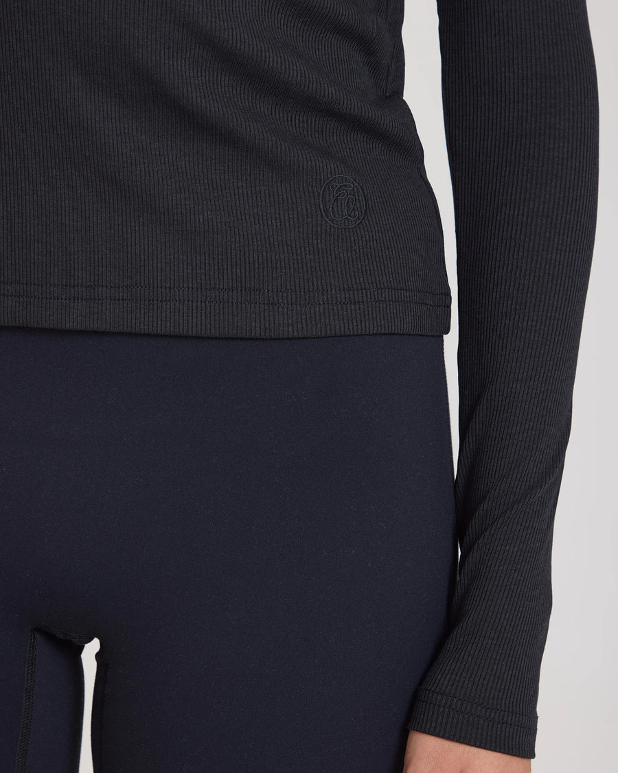 Close-up of Emello's black Forma ribbed turtleneck top highlighting the intricate textured fabric and slim fit.