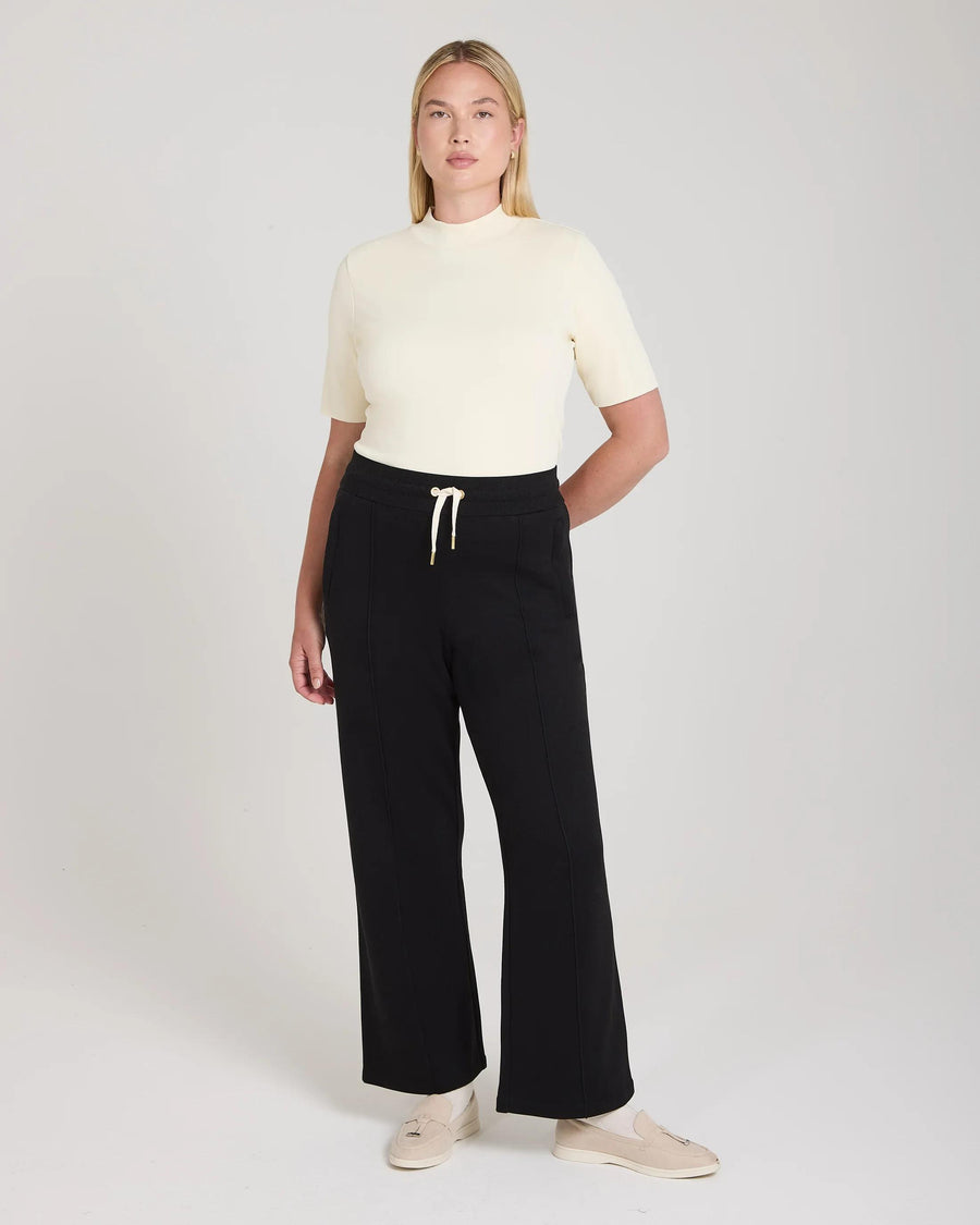 Model wearing Emello black wide-leg lyocell trousers with pin-tuck detailing, featuring a cream top.
