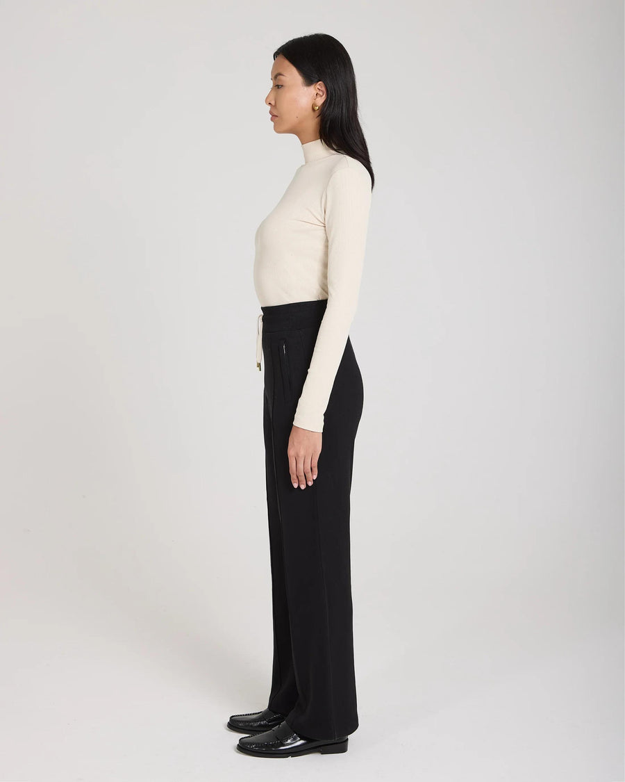 Side view of model wearing black wide-leg lyocell trousers with pin-tuck detailing