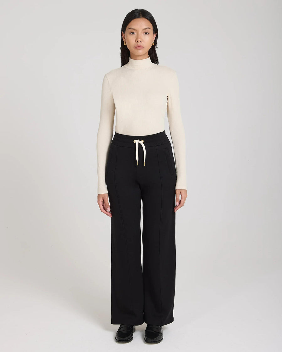 Model wearing Emello black wide-leg lyocell trousers with pin-tuck detailing and drawcord waistband.