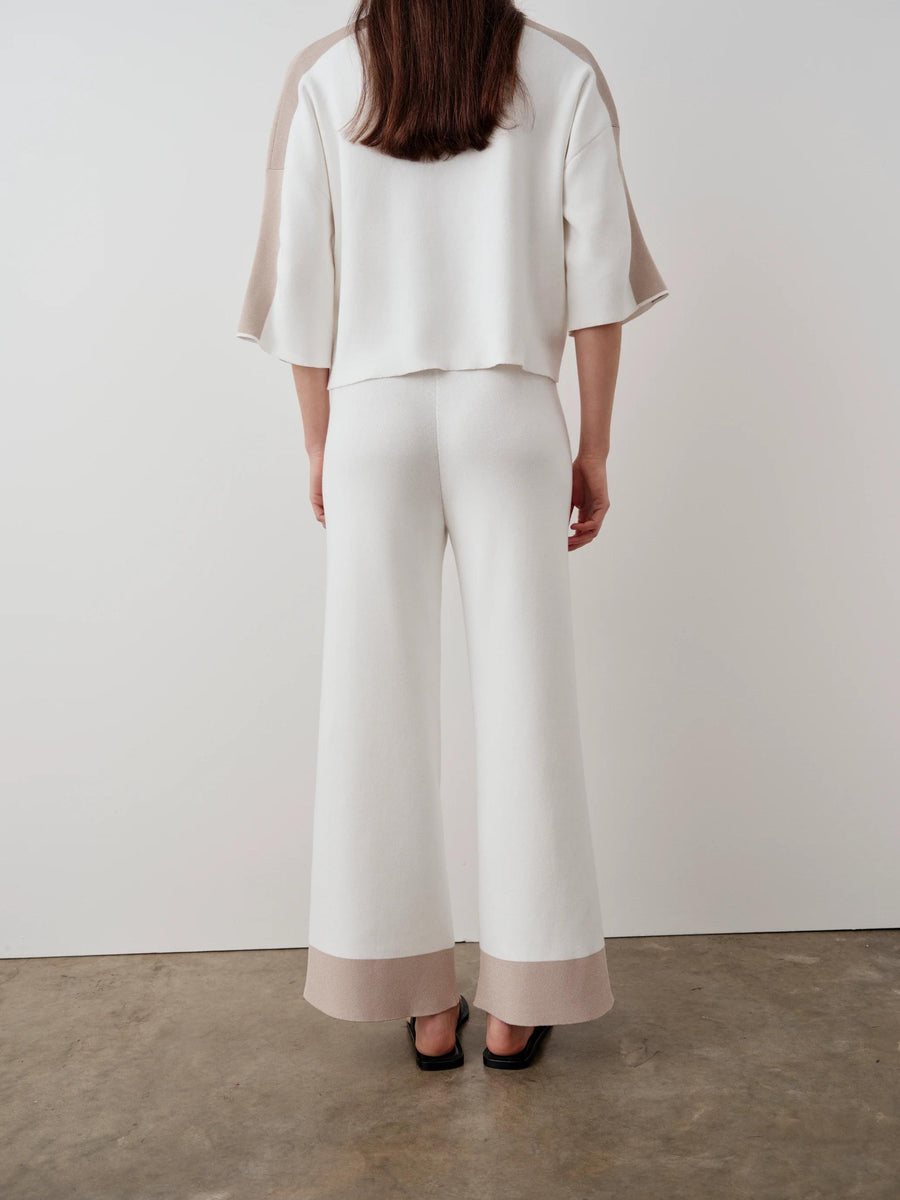 Rear view of a woman wearing Emello's contrast hem wide leg trousers in white, showcasing the elegant drape and unique hem detail.