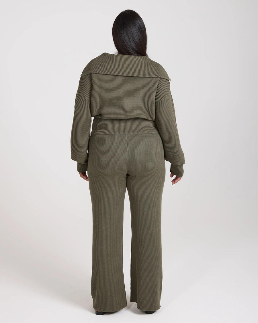 Back view of model wearing olive green ribbed knit wide leg trousers with relaxed fit.